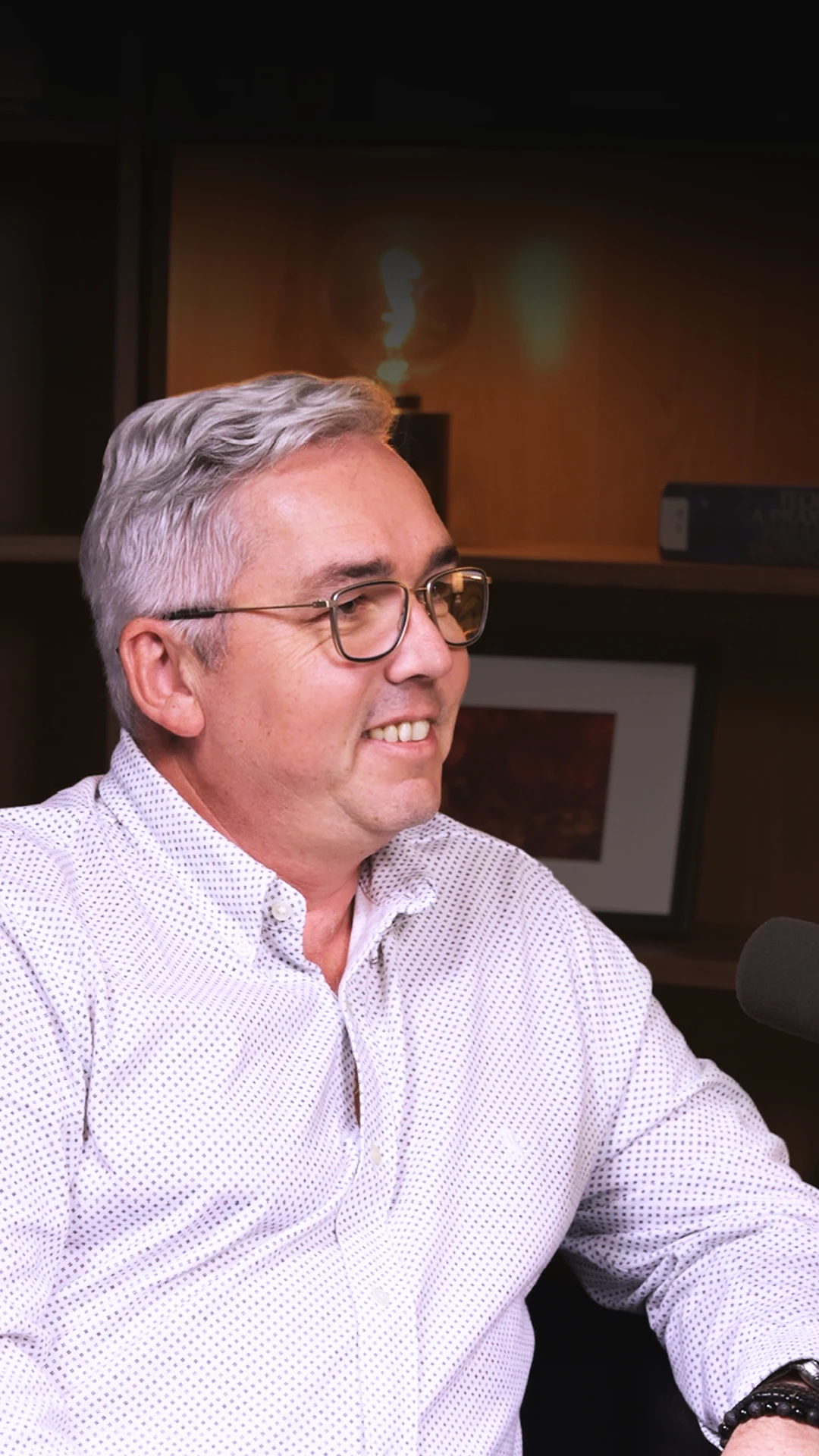 Muž v košili a brýlích sedící v křesle v podcastovém studiu